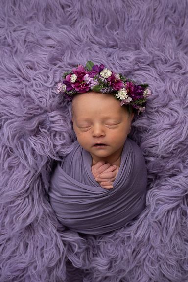 Sleeping newborn baby wrapped in purple with a floral headband