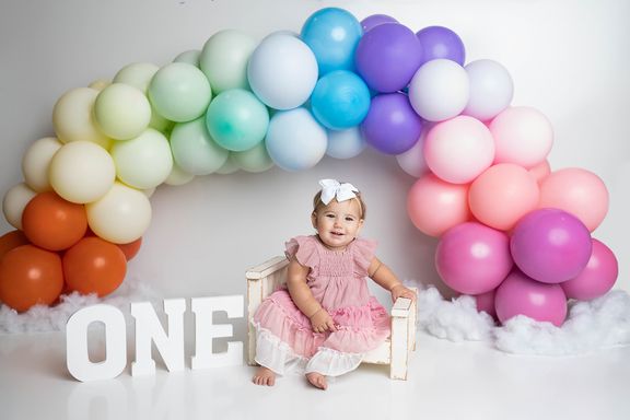 Baby girl sitting in front of colorful balloons during her first birthday session