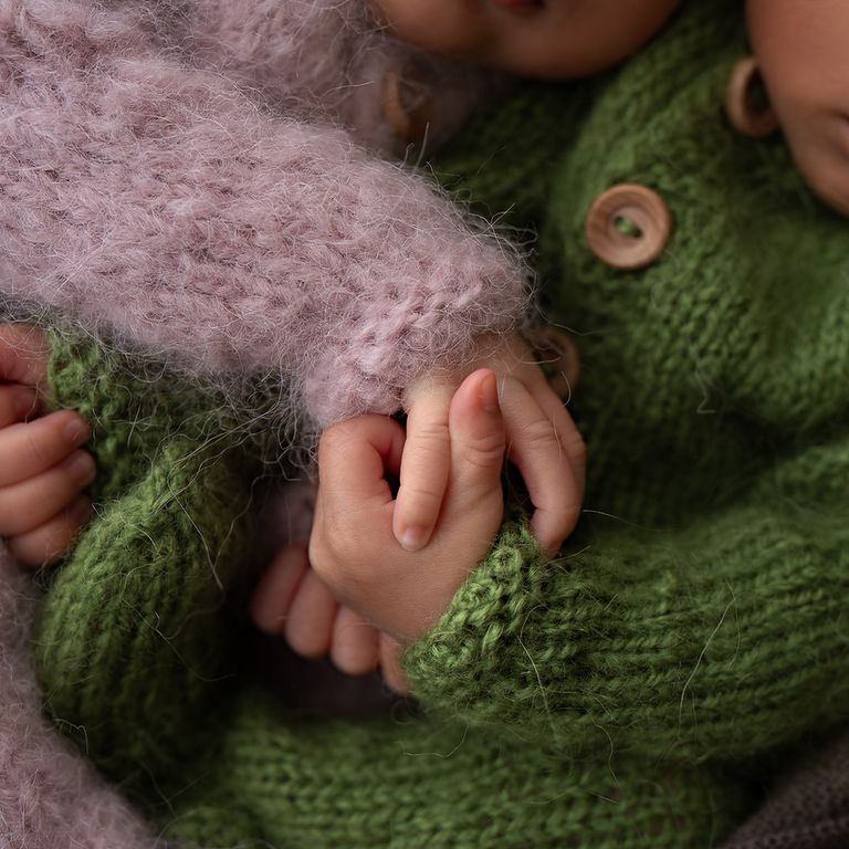Close-up of newborn twins holding hands while wrapped in soft pink and green
