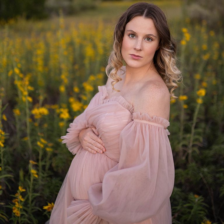 Expecting mother in a blush pink dress photographed outdoors among wildflowers during a maternity session