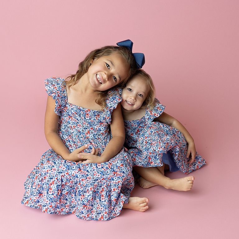 Two sisters smiling together in matching floral dresses during a studio childhood portrait session
