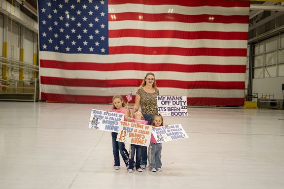 Children holding handmade signs while waiting for their military parent to come home