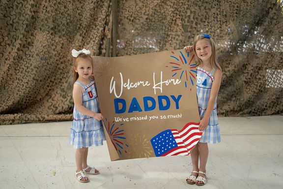 Children holding a Welcome Home Daddy sign before a military homecoming