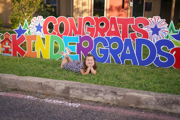 Kindergarten graduate celebrating with a colorful graduation yard sign